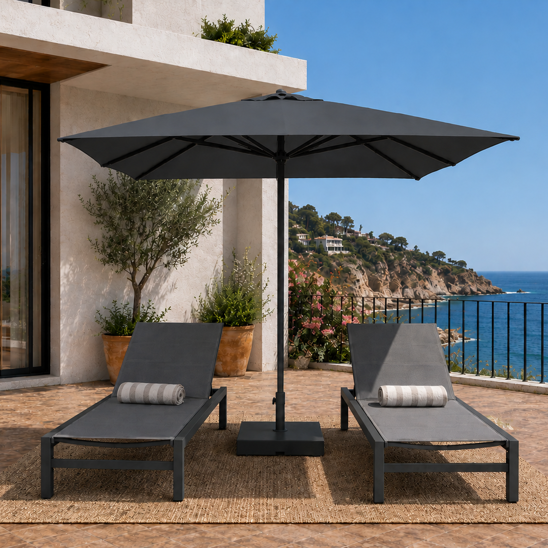 Two gray lounge chairs with a black umbrella on a patio overlooking the ocean.
