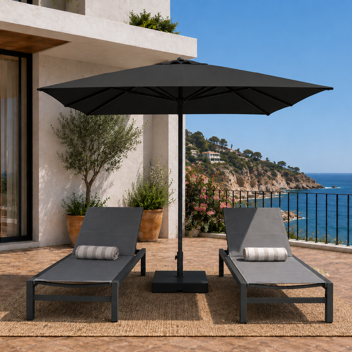 Two gray lounge chairs under a black patio umbrella on a wooden deck with ocean view.