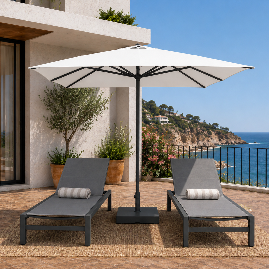 Outdoor patio with two lounge chairs and a large umbrella overlooking a scenic ocean view.