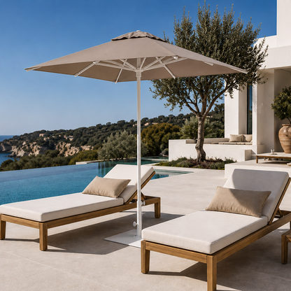 Two wooden lounge chairs with beige cushions under a large umbrella by a pool with ocean view.